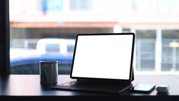 istock Mock up tablet computer with blank screen, coffee cup and smartphone on blank wooden desk. Blank screen for graphics display montage. 1293592228