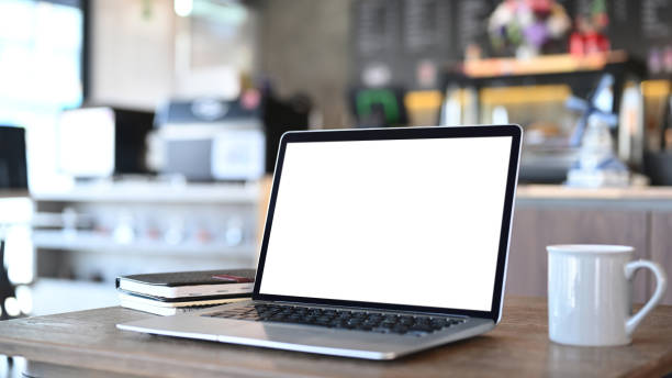 istock An open laptop computer with blank screen, coffee cup and notebook on wooden desk. Blank screen for graphics display montage. 1293592322