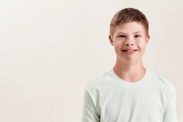 istock Portrait of cheerful disabled boy with Down syndrome smiling at camera while posing isolated over white background 1293593352