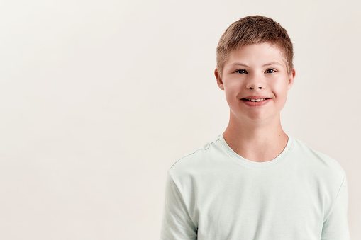 Portrait of cheerful disabled boy with Down syndrome smiling at camera while posing isolated over white background. Children with disabilities and special needs concept. Horizontal shot