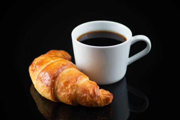 istock Croissant and White Cup of Coffee on Black Reflective Background 1293595110