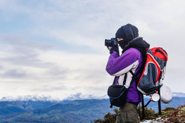Well wrapped nature photographer with backpack taking pictures of a snowy landscape. hiker in the mountain.