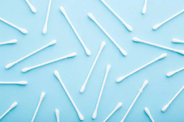 Photo of White sticks of cotton bud on light blue table background. Pastel color. Closeup. Top down view.