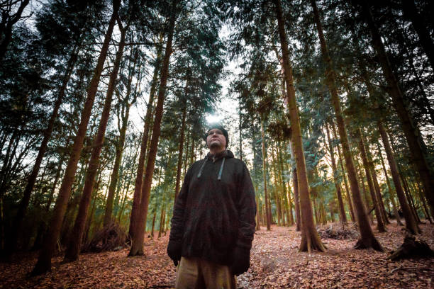 Young man with rifle and hat walking through woodland, holding hand and protecting himself of sun