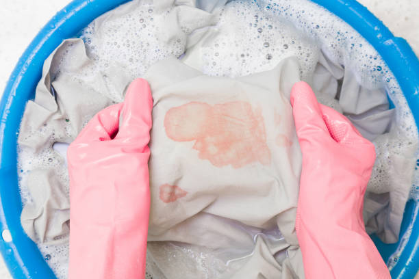 Hands in rubber protective gloves washing sheet with blood stain in blue basin. Point of view shot. Closeup. Top down view. stock photo