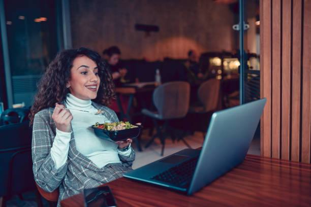 istock Cute Female Taking Time With Her Salad While Watching Show On Laptop In Restaurant 1293600771
