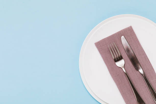 istock Cutlery and napkin in a white ceramic plate on a blue background with copy space, top view 1293604521