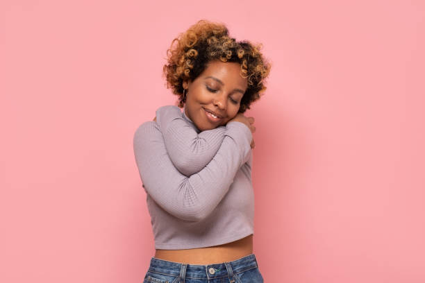 African american woman hugging herself being happy and positive, smiling confident stock photo