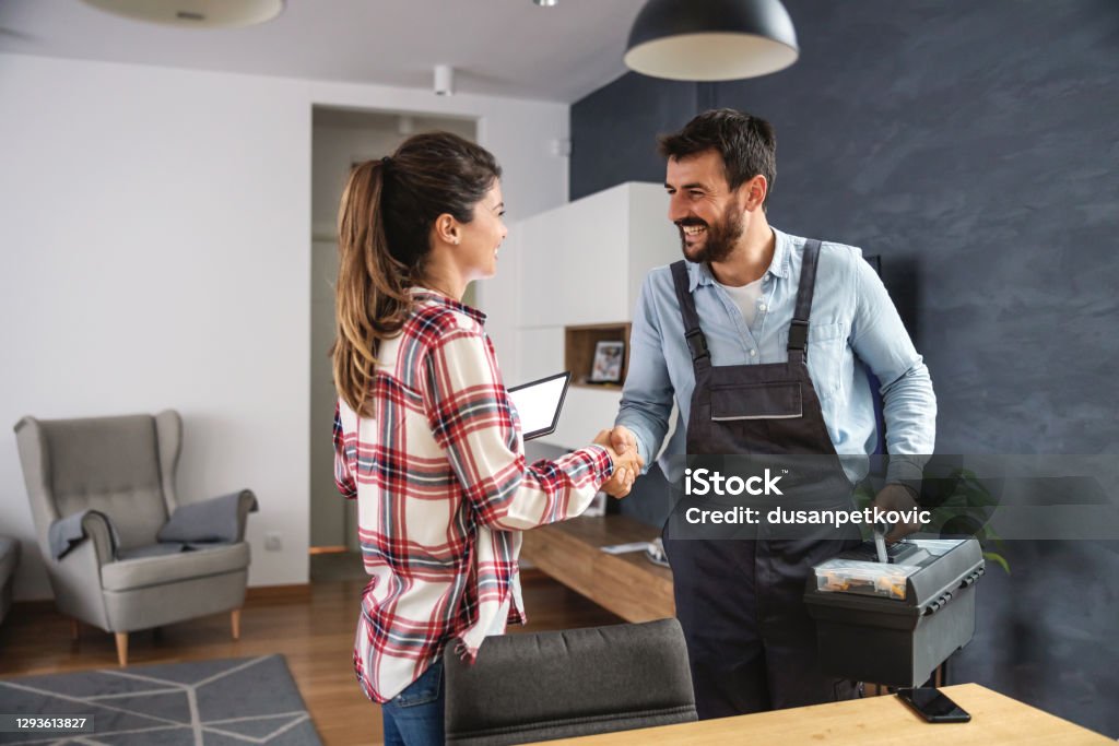 Happy woman shaking hands with repairman. Home interior. Building Contractor Stock Photo