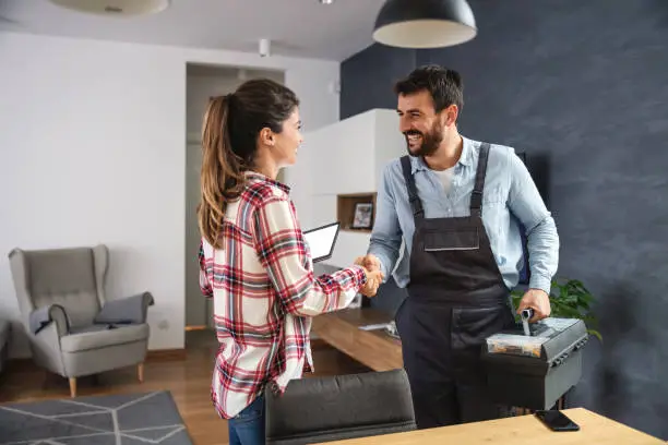 Photo of Happy woman shaking hands with repairman. Home interior.