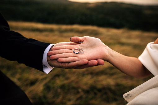 Close-up of wedding rings with hands holding by bride and groom outdoor