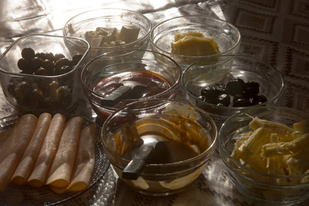 Homemade delicious, daily breakfast table at home. Rosehip marmalade, tahini molasses, cheese, black and green olives, butter, smoked turkey slices. Horizontal close-up.