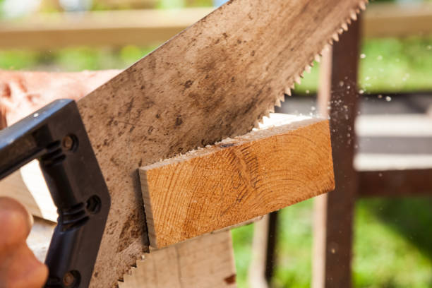 istock A metal hand saw with a black plastic handle with sharp teeth in the hands of a carpenter when sawing wooden beams with small chips flying to the sides. on a summer day. Construction on a cottage. 1293618292