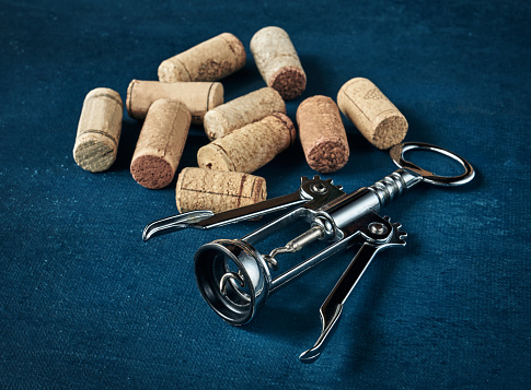 Corkscrew and used bottle corks on a dark background, shallow depth of sharpness