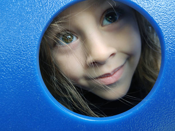istock Young girl peeking through blue playground slide 1293619944