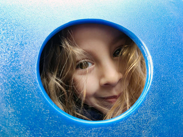 istock Young girl peeking through blue playground slide 1293619955