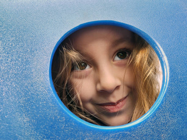 istock Young girl peeking through blue playground slide 1293619961