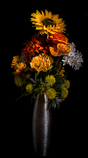 Bouquet of autumn yellow, orange and white flowers in a silver vase isolated against a black background.