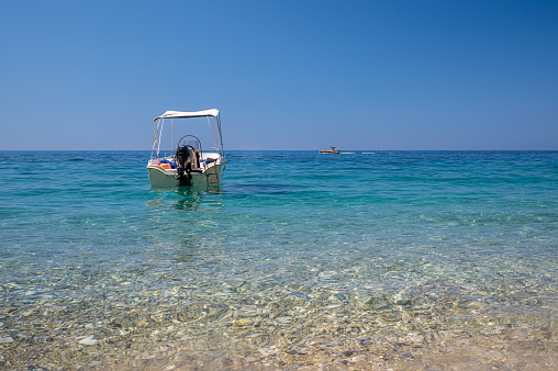 A small motorboat, floating in the crystal clear Mediterranean sea, off the coast of a Greek island