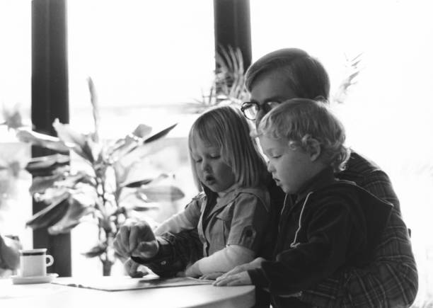 Vintage young father with daughter and son reading a comic book. 1977 vintage, seventies, retro monochrome image of a young father with daughter and son reading a comic book. dutch culture photos stock pictures, royalty-free photos & images