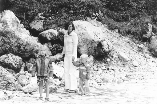 1977 vintage, seventies, retro monochrome image of young mother with son and daughter driving a vintage car in  Lido di Jesolo near Venice, Italy.