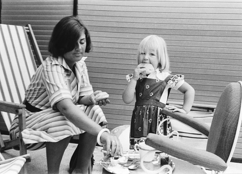 1976 vintage, seventies, retro monochrome image of  a young mother with daughter eating white buns with tea in the summer sun.