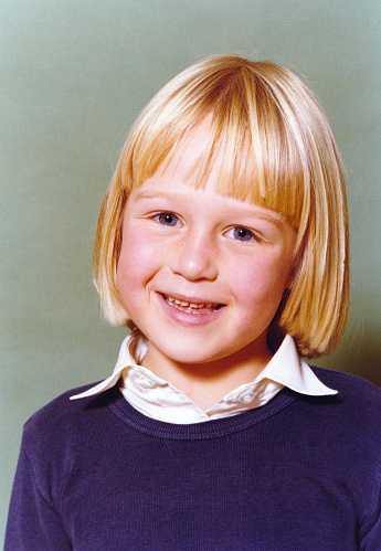 Vintage 1981 yearbook school image of a smiling young girl with blond hair and blue eyes with blue sweater and white blouse.