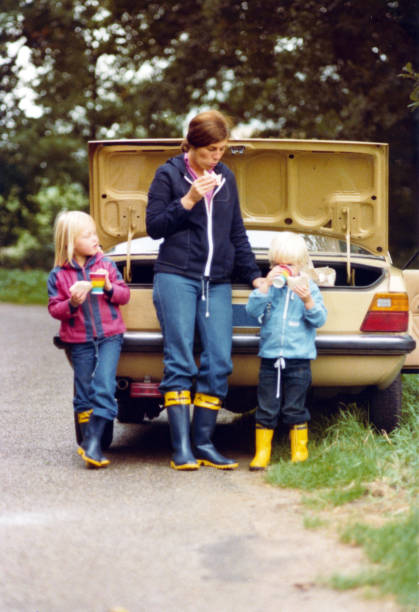 giovane madre con figlio e figlia che mangiano un panino in natura, davanti a un'auto. - car family picnic vacations foto e immagini stock