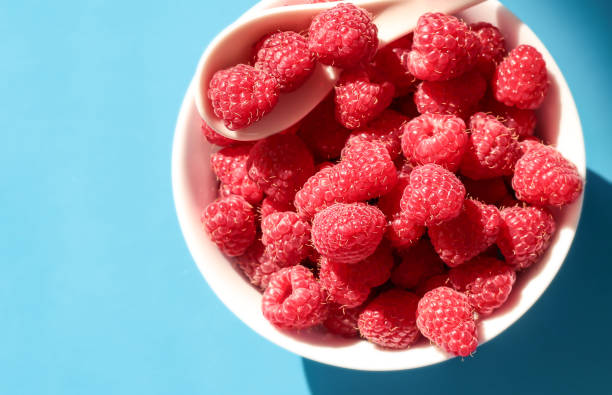 istock Ripe raspberries in a white plate on a blue background. On a white spoon raspberries. 1293622819