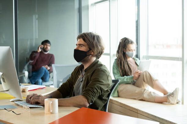 istock Young businessman in black protective mask and casualwear using computer 1293625566