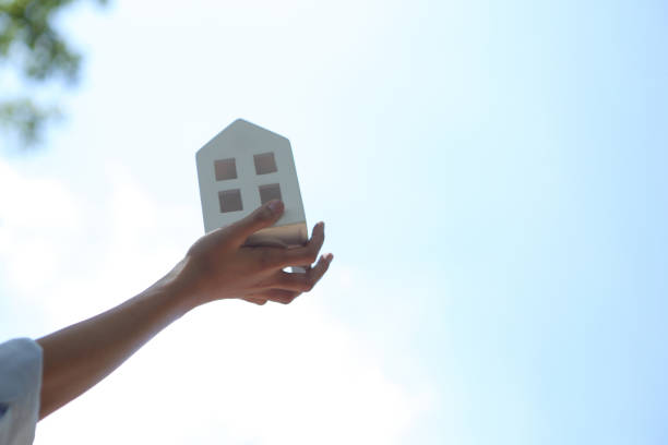 istock Hand holding white house with blue sky background 1293625687