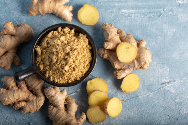 istock Fresh ginger root and ground ginger spice in black bowl on blue background. 1293626956
