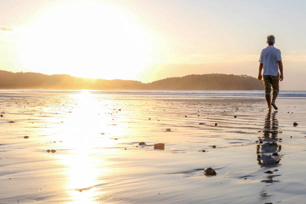 istock Man walks barefoot down sandy beach at sunrise 1293629837