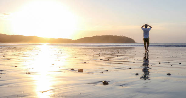 istock Man walks barefoot down sandy beach at sunrise 1293629963