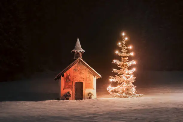Christmas tree near tiny snow covered chapel hidden in the woods