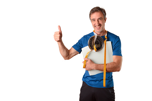 Man with weighing scale and measuring tape hanging dressed in sportswear and isolated white background.