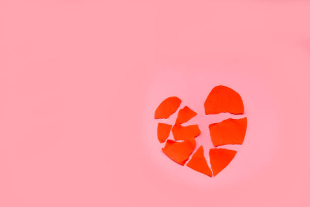 symbol valentines day - red heart is broken, closeup on pink background.