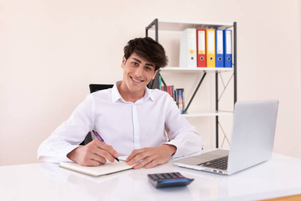istock Happy young businessman taking notes and looking at camera and smiling 1293641986