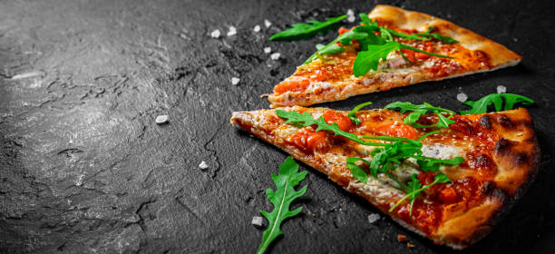 モッツァレラチーズ、サーモンフィッシュ、トマトソース、ルッコラとピザの2つのスライス。ダークグレーの黒いスレートの背景にイタリアのピザ - pizza tuna prepared fish cheese ストックフォトと画像