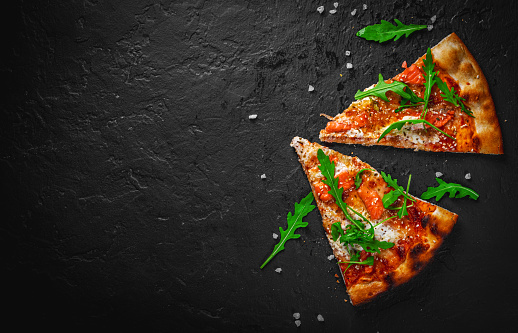 two slice of Pizza with Mozzarella cheese, salmon fish, tomato sauce, arugula. Italian pizza on Dark grey black slate background