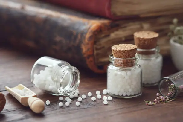 Photo of Bottles of homeopathic globules and old books. Homeopathy medicine concept.