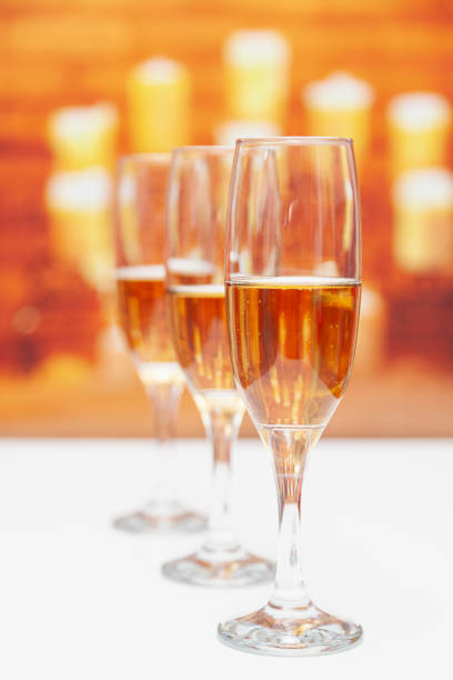 Three glasses of champagne, one of them is in focus Three glasses of champagne on a white table, the first is in focus. The background is out of focus, one can sense that it is a fireplace with burning candles. rose champagne stock pictures, royalty-free photos & images
