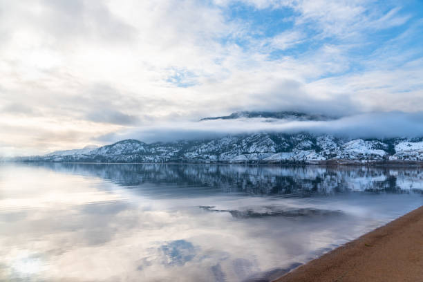 istock Snow covered mountain, fog, clouds, and sunlight reflected in calm lake 1293650683