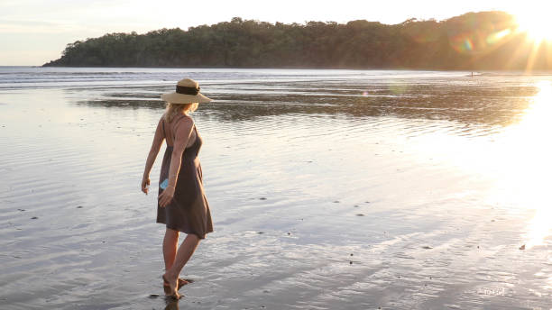 istock Woman walks down sandy beach coastline at sunrise 1293650984