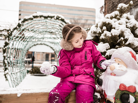 Young girl on a urban street with snow. Winter holiday in the city.