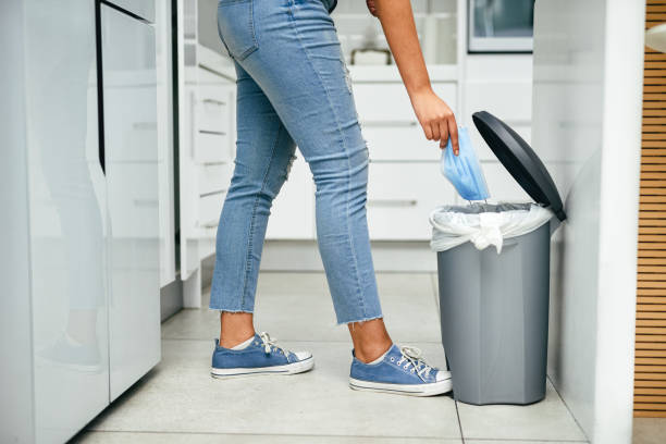 It's part of keeping coronavirus out of your home Closeup shot of an unrecognisable woman disposing a mask in a bin at home pedal bin stock pictures, royalty-free photos & images