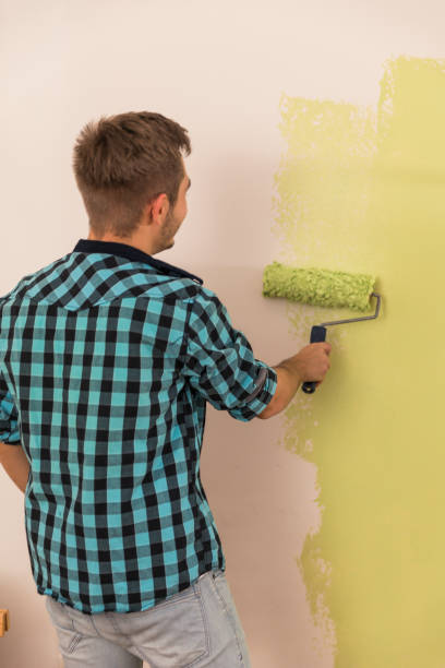 istock Young man using a paint roller to apply green paint on a wall 1293659603
