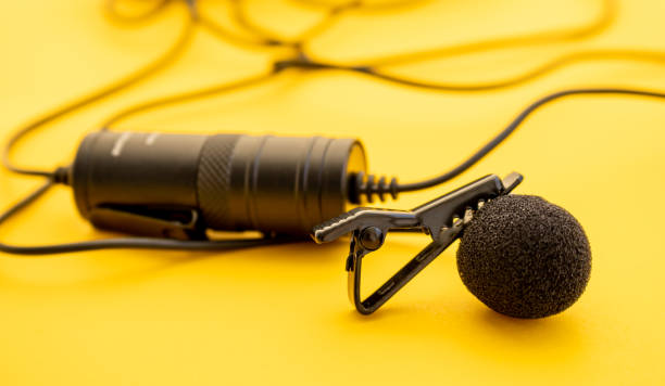 istock Professional lavalier or lapel microphone on a colored surface, very close-up. Details of the grip clip or fastener, mic power bank, miniplug, and wind sponge are visible. Concept useful object, sound production, 1293659611