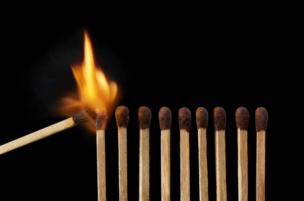 Burning match setting fire to its neighbours isolated on black stock photo