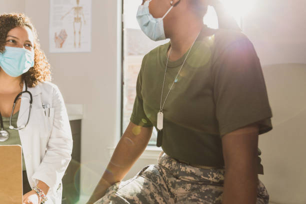 Female gynecologist smiles through mask at female army soldier The mid adult female gynecologist and the mid adult female army soldier smile at each other through their protective masks during COVID-19. womens issues photos stock pictures, royalty-free photos & images